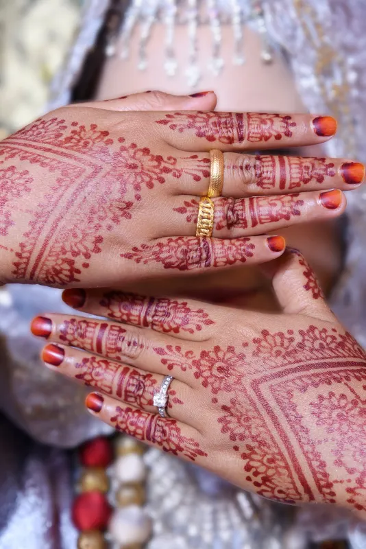 Bride's hennaed hands with gold rings and a diamond solitaire held before her face